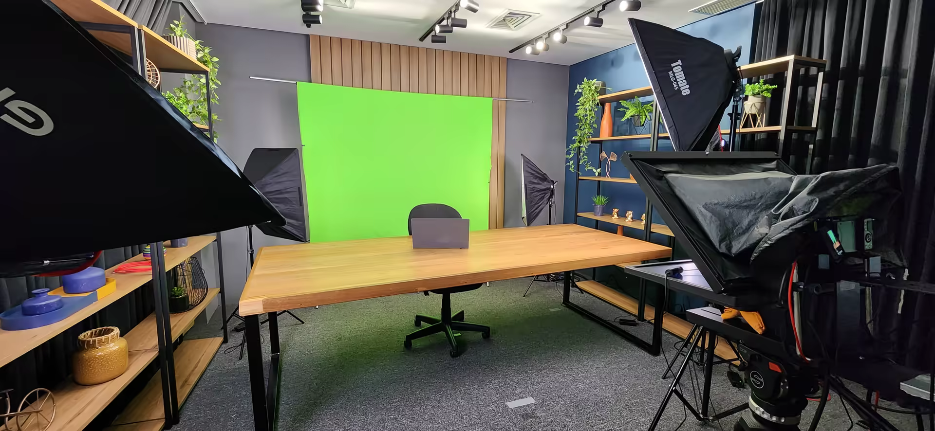 Sala com fundo verde, teleprompter e mesa preparada para gravação de videoaula