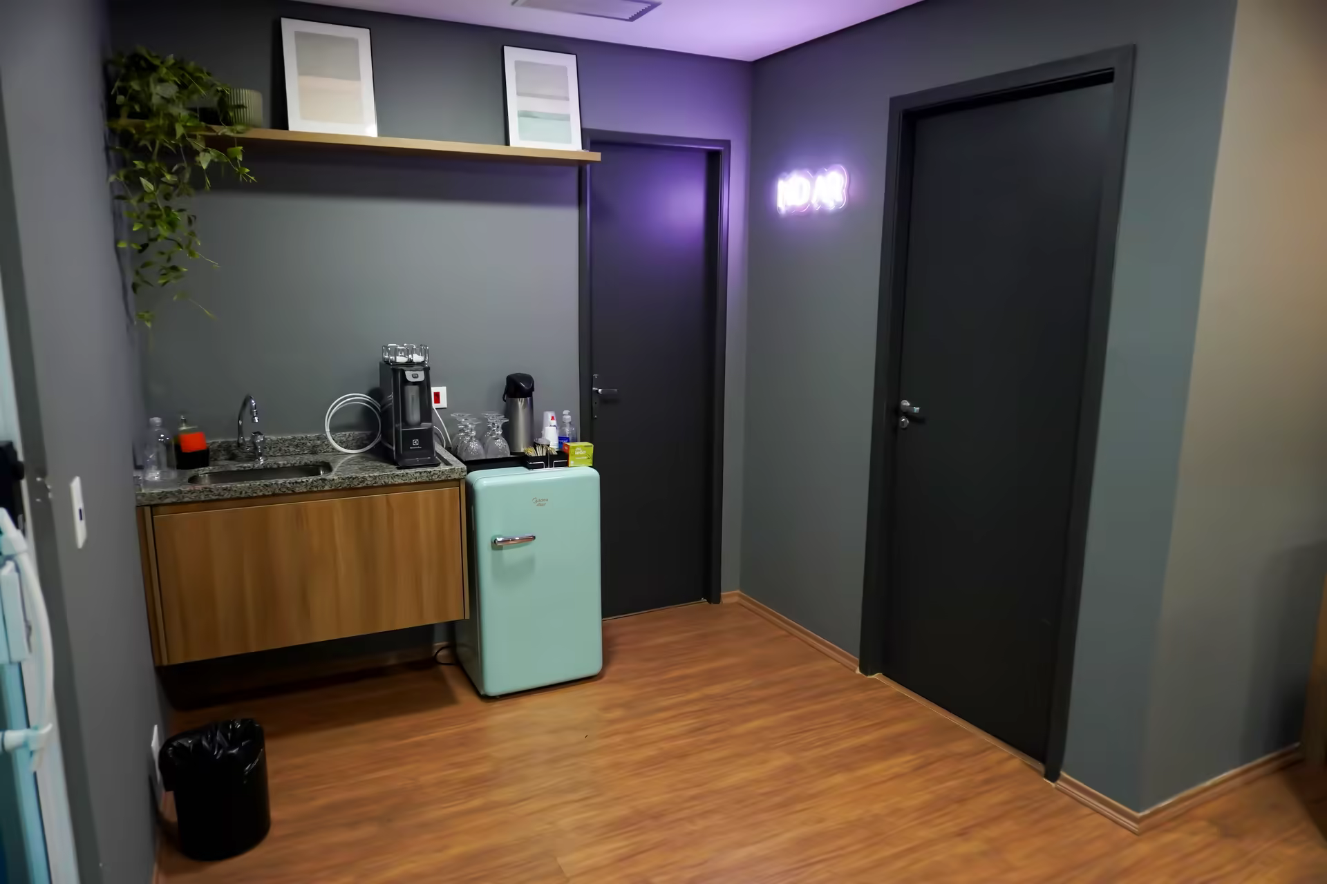 Área de apoio com copa, frigobar e letreiro neon NO AR