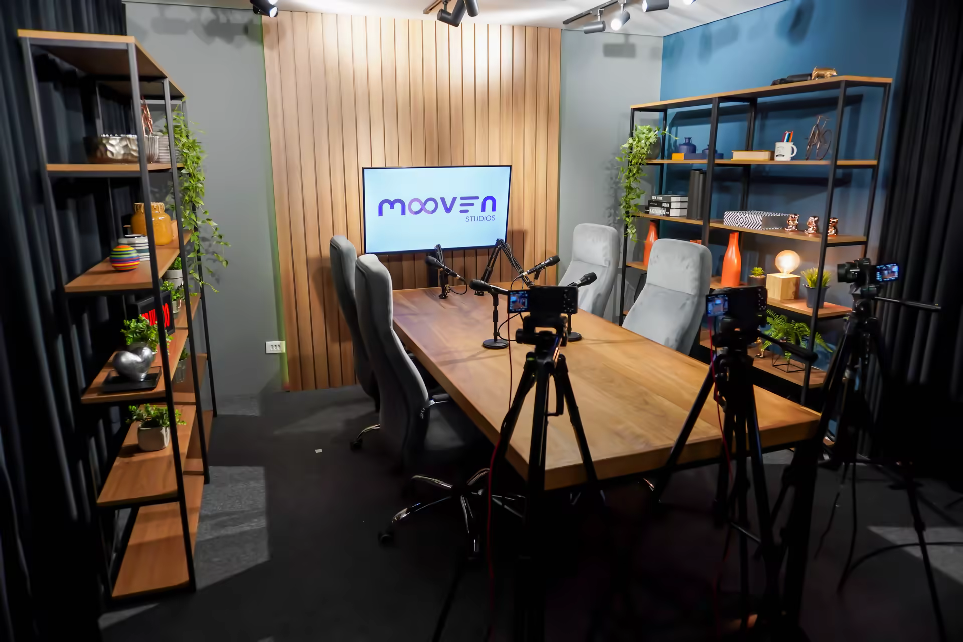 Cenografia do estúdio com bancada de madeira, estantes e TV com a marca Mooven Studios